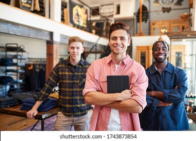 Portrait Of Smiling Multi-Cultural Male Sales Team In Fashion Store In Front Of Clothing Display