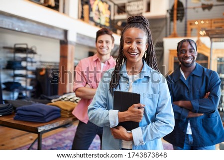 Portrait Of Smiling Multi-Cultural Sales Team In Fashion Store In Front Of Clothing Display