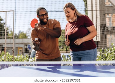 Portrait of smiling multiethnic couple playing ping pong table tennis outdoors - Powered by Shutterstock