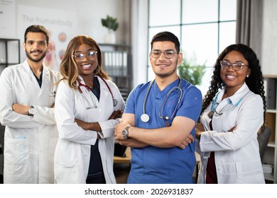 Portrait Of Smiling Multiethnic Medical Team Standing In Modern Clinic Room With Arms Crossed. Group Of Pleasant Confident Skilled Multiracial Physicians Posing Indoors With Arms Folded