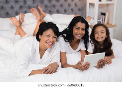 Portrait of smiling multi-generation family using digital tablet while lying on bed at home - Powered by Shutterstock