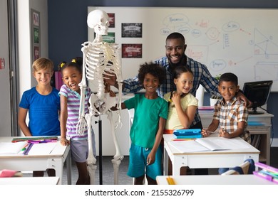 Portrait Of Smiling Multiracial Students And African American Young Male Teacher With Skeleton. Unaltered, Education, Childhood, Teaching, Science, Stem And School Concept.