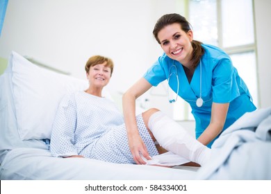 Portrait Of Smiling Nurse Bandaging Leg Of Patient In Hospital