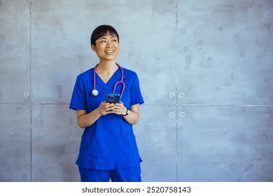 Portrait of a smiling nurse in blue scrubs, holding a smartphone indoors, showcasing modern healthcare communication and professionalism. - Powered by Shutterstock