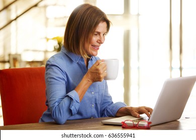 Portrait Of Smiling Older Woman Drinking Coffee And Looking At Laptop