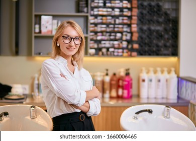 portrait of smiling open-minded consultant of beauty saloon selling beauty products, different shampoos and balms. Blond woman in white shirt and eye glasses stand isolated in beauty saloon - Shutterstock ID 1660006465