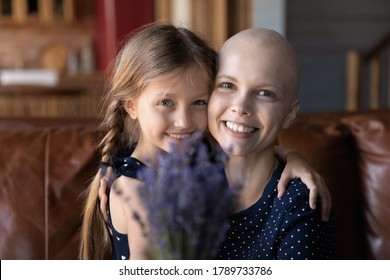 Portrait Of Smiling Optimistic Young Caucasian Sick Cancer Patient Mom And Little Daughter Hug Pose With Flowers, Happy Ill Bald Hairless Mother And Small Girl Child Hug Embrace Show Love And Care