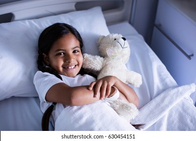 Portrait of smiling patient relaxing on bed with teddy bear in hospital - Powered by Shutterstock