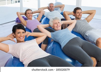 Portrait of smiling people stretching on exercise balls in the bright gym