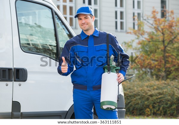 Portrait of smiling pest control worker showing\
thumbsup while standing by\
truck