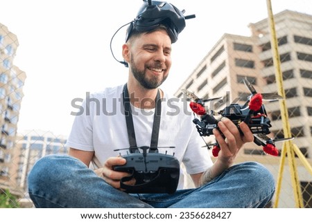 Portrait of smiling pilot man weraing goggles and holding remote controller and fpv drone in hands. Multicopter operating experience, unmanned aviation concept.