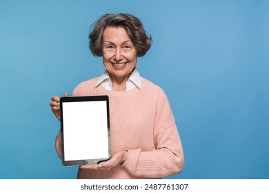 Portrait of smiling positive senior old mature woman female pensioner with tablet computer pc pad, grandmother using holding demonstrate showing tablet screen isolated on blue background. - Powered by Shutterstock