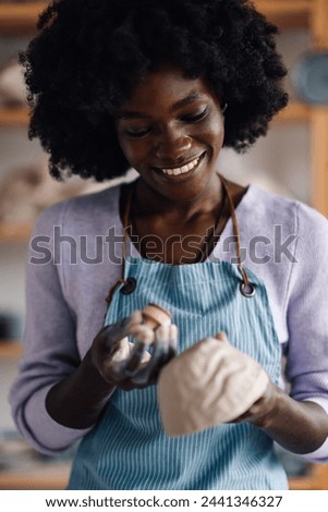 Portrait of a smiling pottery class student standing at modern workshop and imprinting and decorating clay work. An african american craftswoman decorating and imprinting earthenware at pottery studio