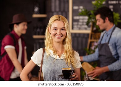 Portrait von lächelnden, hübschen Kunden, die eine Tasse Kaffee in der Kaffeerei halten