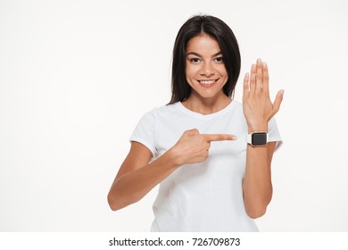 Portrait Of A Smiling Pretty Woman Pointing Finger At Smart Watch On Her Wrist Isolated Over White Background