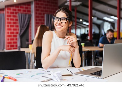 Portrait of smiling pretty young business woman in glasses sitting on workplace - Shutterstock ID 437021746