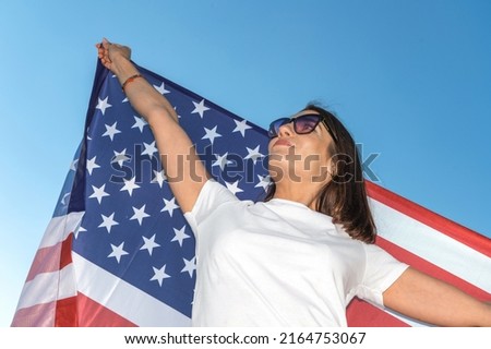 Portrait of smiling pretty young woman holding waving American flag. USA celebrate 4th of July. Patriotic young woman flies an american flag on a beautiful field. 