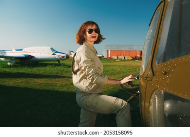 Portrait Of A Smiling Professional Helicopter Pilot With Bright Red Lips And Black Sunglasses Posing By Her Aircraft Before The Flight. 