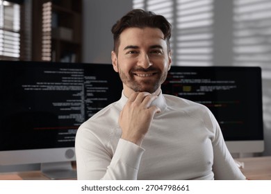Portrait of smiling programmer in front of computer with dual monitors at workplace