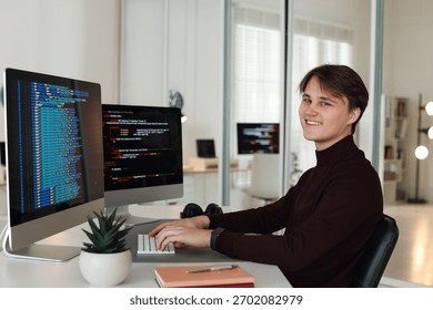 Portrait of smiling programmer working on computer with dual monitors at white table in office