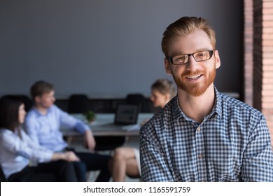 Portrait Of Smiling Red Haired Male Employee Look At Camera During Business Meeting In Office, Happy Man In Glasses Pose For Corporate Photoshoot, Worker Or Team Leader Making Picture During Briefing