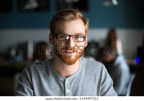Portrait\
of smiling red haired millennial man looking at camera sitting in\
café or coffeeshop, happy young male in glasses posing for picture\
working at laptop or studying out in\
coffeehouse