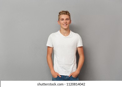 Portrait of a smiling relaxed teenage boy looking at camera while standing over gray background