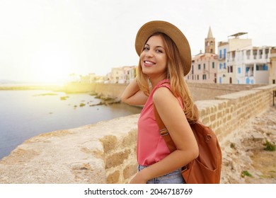 Portrait of smiling relaxed traveler woman walking along Alghero seafront, Sardinia, Italy
