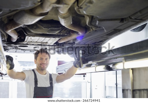 Portrait of smiling repair worker examining car\
in workshop