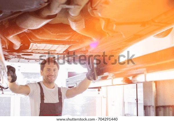 Portrait of smiling repair worker examining car\
in workshop