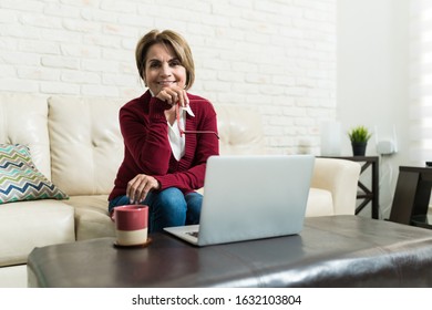 Portrait of smiling retired woman sitting with laptop in living room