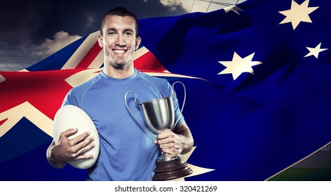 Portrait of smiling rugby player holding trophy and ball against rugby stadium - Powered by Shutterstock
