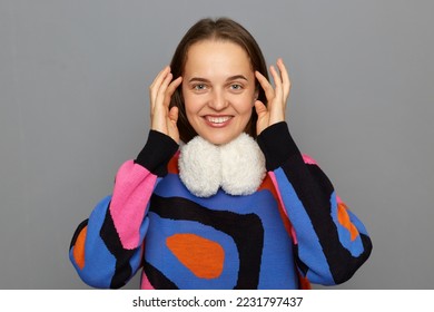 Portrait of smiling satisfied delighted woman with brown hair wearing colorful jumper posing isolated over gray background, touching her hair, looking at camera, expressing happiness. - Shutterstock ID 2231797437