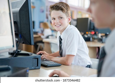 Portrait Of A Smiling School Boy Wearing Uniform And Using A Computer In The Computer Lab