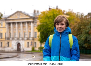 Portrait Of A Smiling Schoolboy With A Backpack On A Rainy Day Outside