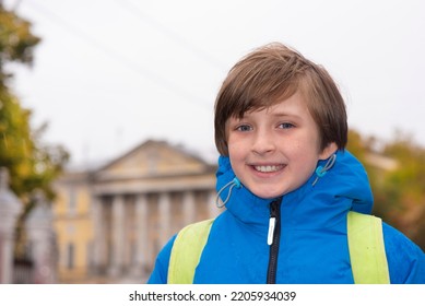 Portrait Of A Smiling Schoolboy With A Backpack On A Rainy Day Outside