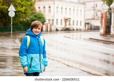 Portrait Of A Smiling Schoolboy With A Backpack On A Rainy Day Outside