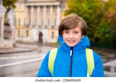 Portrait Of A Smiling Schoolboy With A Backpack On A Rainy Day Outside