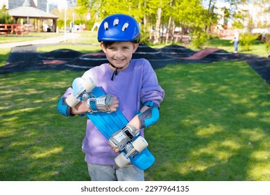 portrait of a smiling schoolboy in a safety helmet with a bright blue skateboard, an urban cruiser in his hands in an outdoor skate park in spring