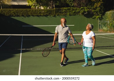 Retrato de una sonriente pareja norteamericana sénior con raquetas de tenis en la pista de tenis. el concepto de jubilación y el estilo de vida activo de los adultos mayores.