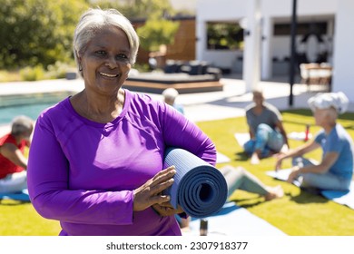 Portrait of smiling senior biracial woman holding yoga mat, with diverse yoga group in sunny garden. Senior lifestyle, active retirement, friendship, health and wellbeing, unaltered. - Powered by Shutterstock