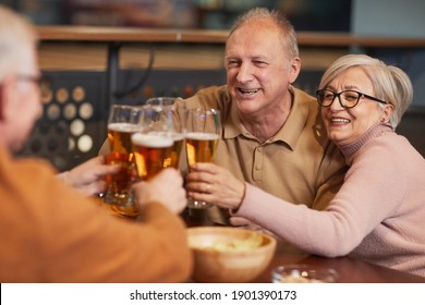 Portrait of smiling senior couple drinking beer in bar and clinking glasses while enjoying night out with friends - Powered by Shutterstock