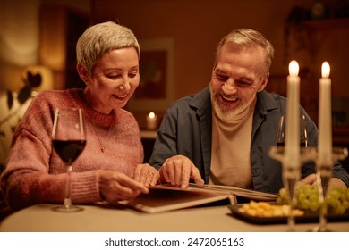 Portrait of smiling senior couple looking at photo album while enjoying romantic date night at home copy space - Powered by Shutterstock