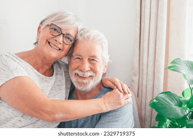 Portrait of smiling senior family couple hugging looking at camera.  Happy white-haired man and woman cuddling embracing sitting at home enjoying moment of affection - Powered by Shutterstock