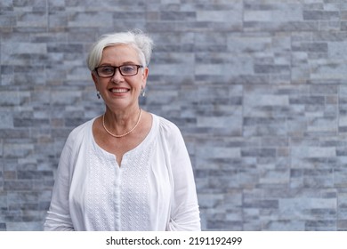 Portrait Of Smiling Senior Female Executive With Short Hair Wearing Eyeglasses And Standing Against Wall Outside Office