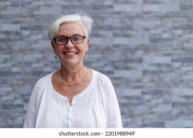 Portrait Of Smiling Senior Female Executive With Short Hair Wearing Eyeglasses And Standing Against Wall Outside Office