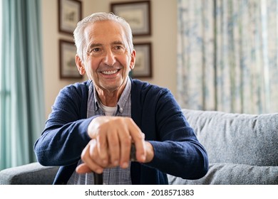 Portrait of smiling senior man holding walking stick sitting on sofa. Cheerful elderly man relaxing at home and holding a support stick with copy space. Happy senior with a big smile at nursing home. - Powered by Shutterstock