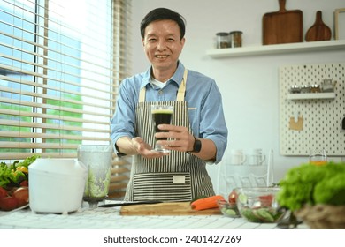 Portrait of smiling senior man holding glass of green smoothie standing in kitchen. Healthy lifestyle concept. - Powered by Shutterstock