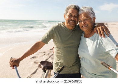 Portrait of smiling senior multiracial couple with arm around bicycles at beach on sunny day. active lifestyle and transportation. - Shutterstock ID 2109660935