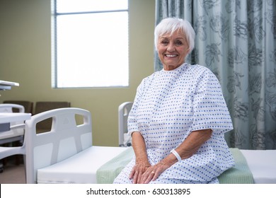 Portrait Of Smiling Senior Patient Sitting On Bed In Hospital